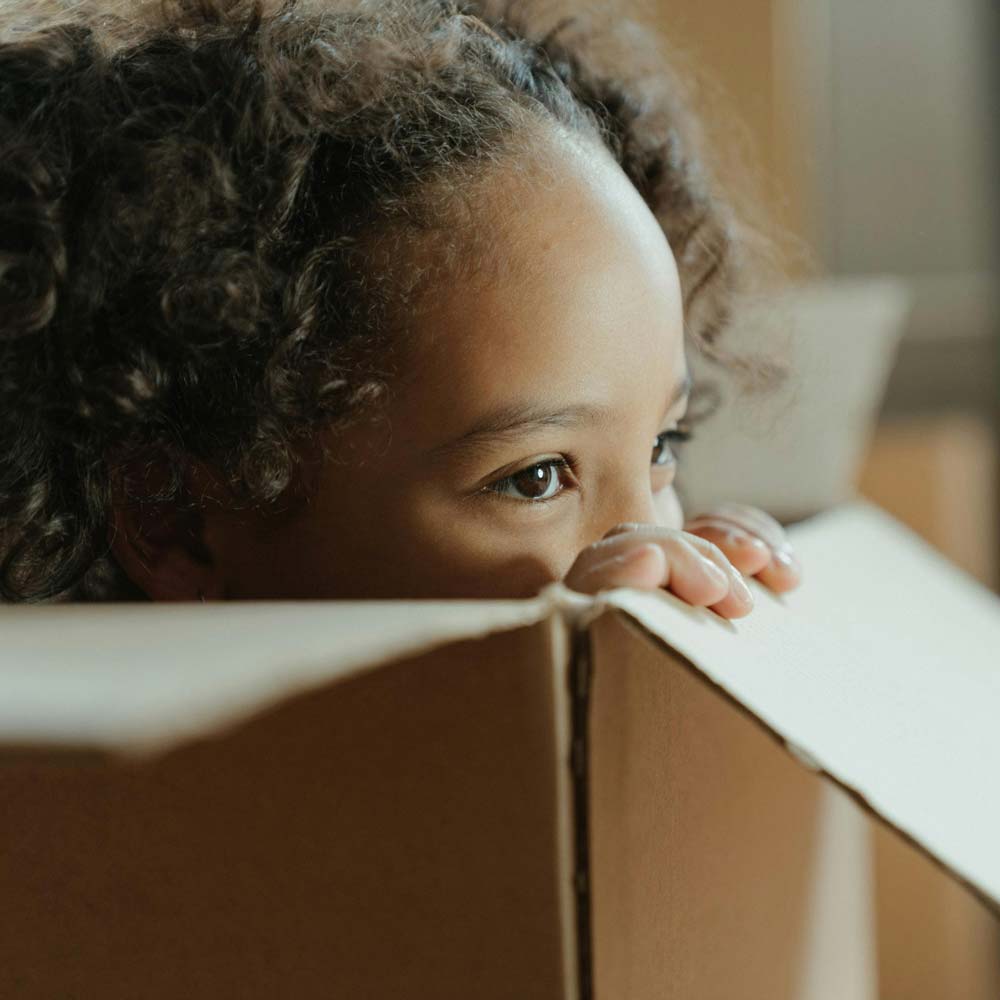 Young child peeking over the top of a cardboard moving box
