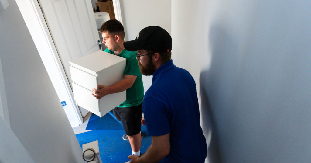 Simply Moving crew carrying a packed box through a doorway